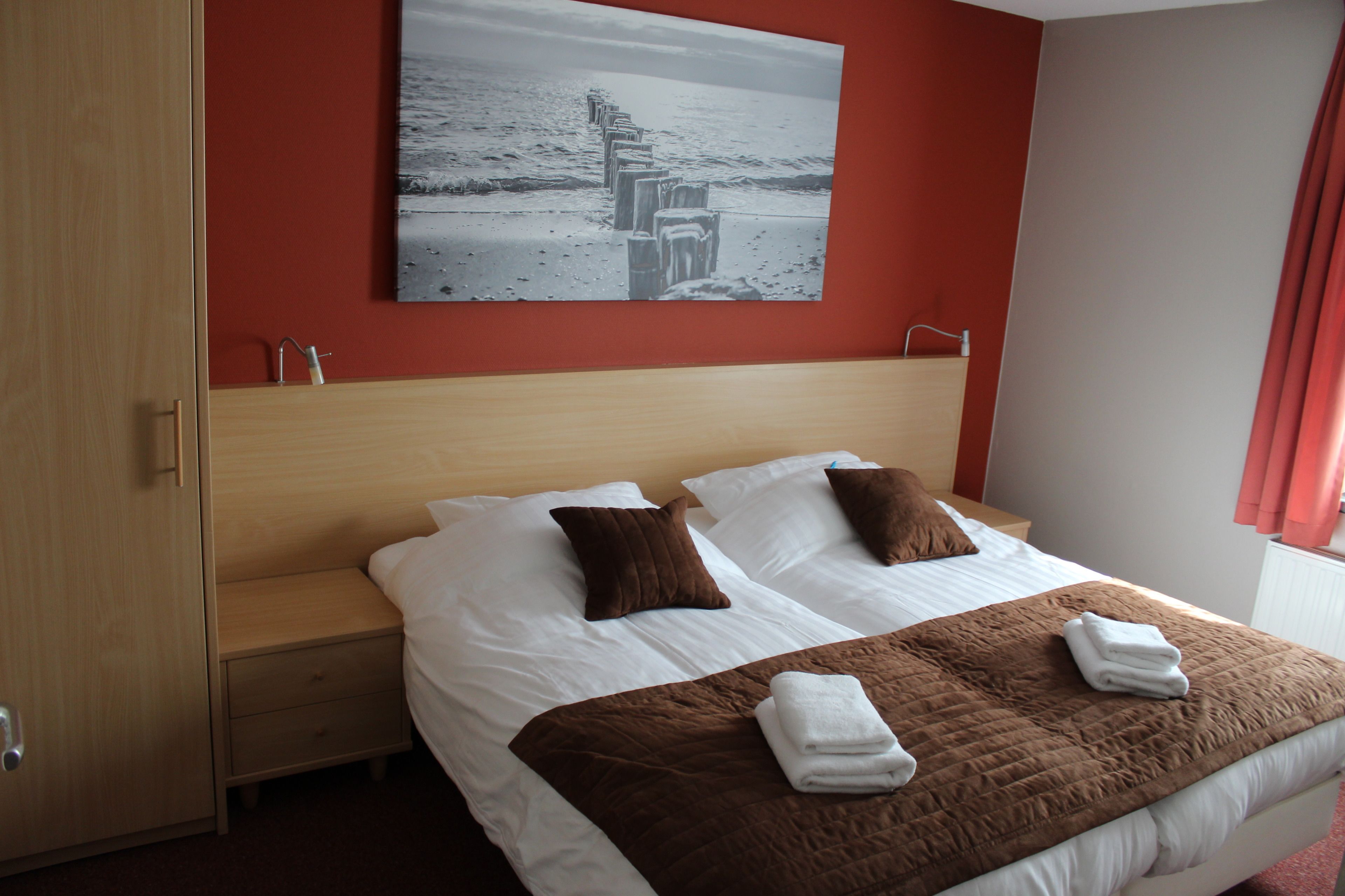 Ein Hotelzimmer mit einem großen Bett, zwei Kissen, einer braunen Decke und einem Bild einer Strandansicht an der Wand.