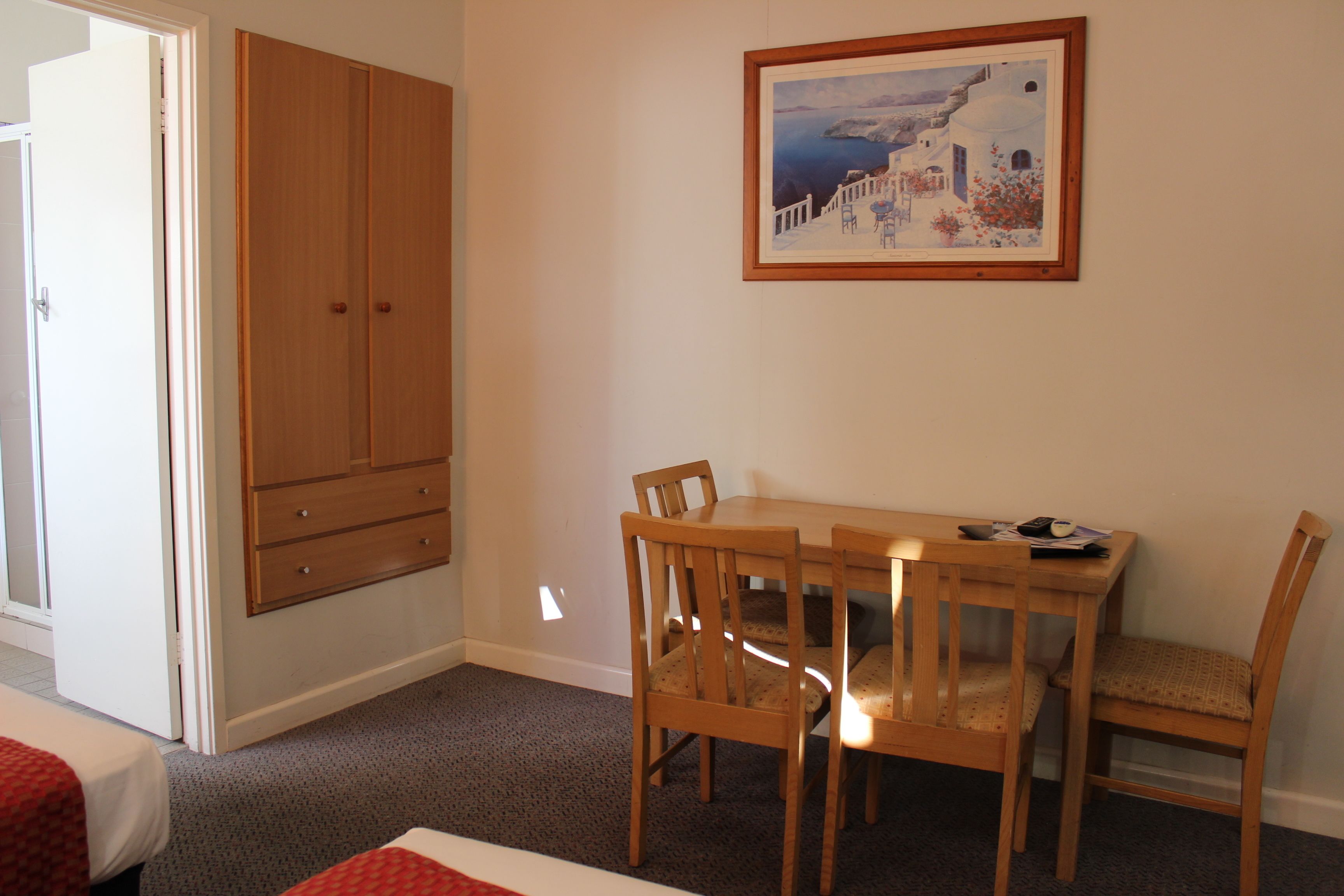 A room with a wooden wardrobe, a dining table with chairs, and a framed painting on the wall.