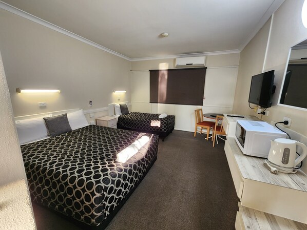 Una habitación de hotel con dos camas, un escritorio, una silla, un televisor y un microondas.