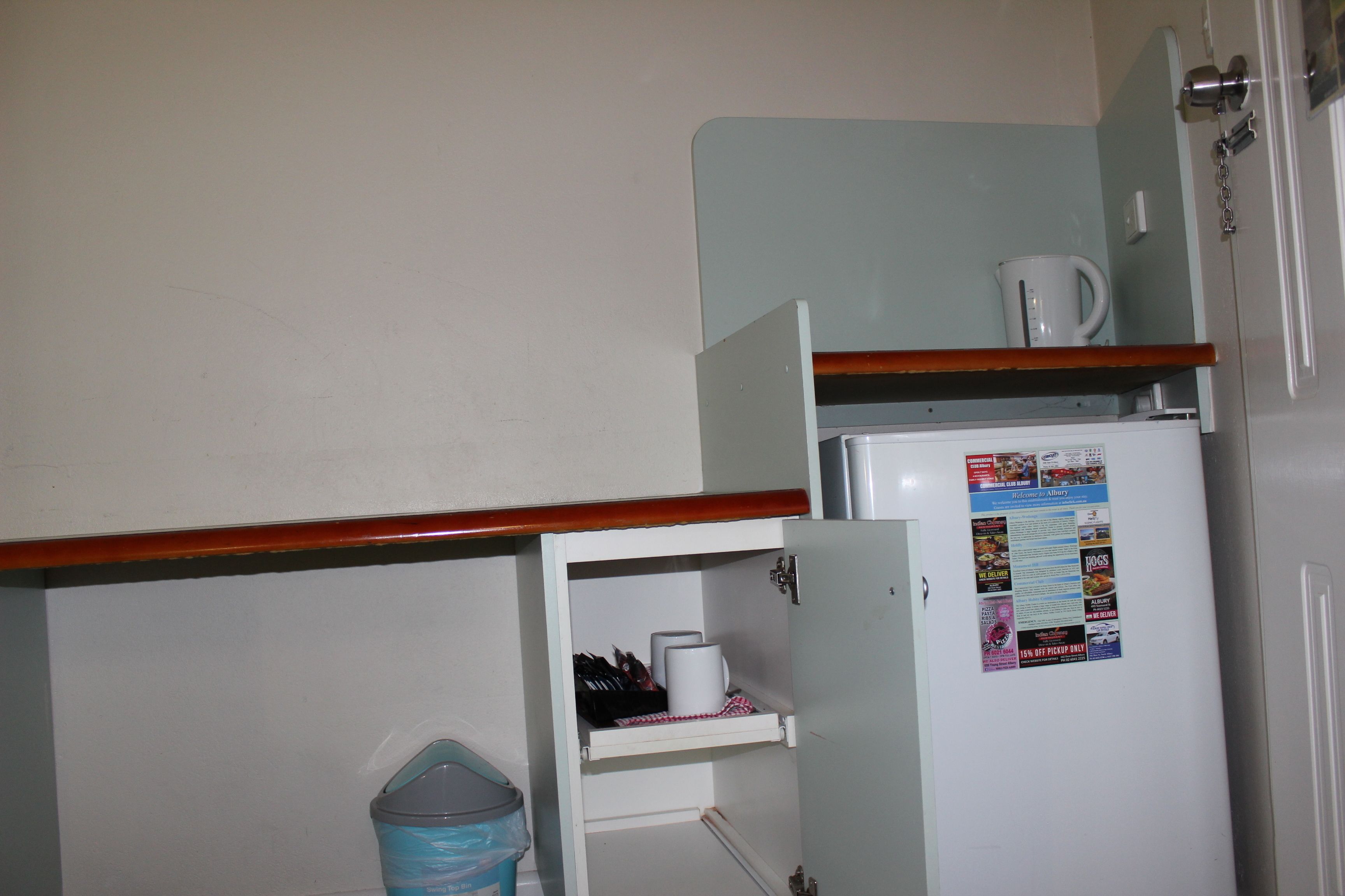 A compact kitchen with a refrigerator, a coffee maker, and a trash bin.