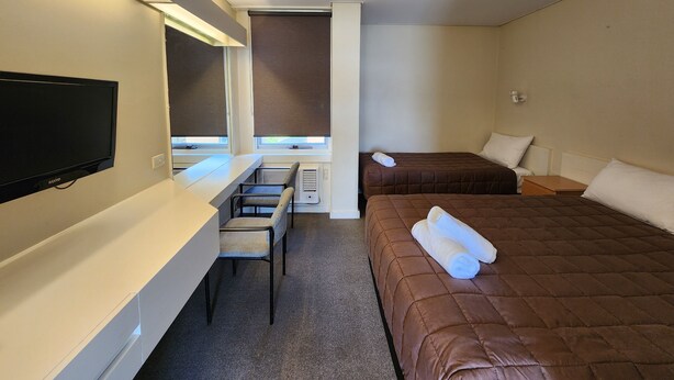 A hotel room with a bed, a desk, a chair, a TV, and a window with blinds. - Hume Inn Motel Albury CBD (South Albury)