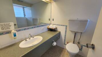 A bathroom with a sink, toilet, and a mirror. A sign instructs to leave the shower curtain inside the shower.