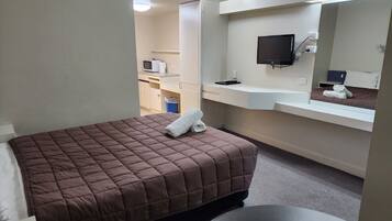 A hotel room with a bed, a small table, a mirror, a TV, and a kitchenette area.