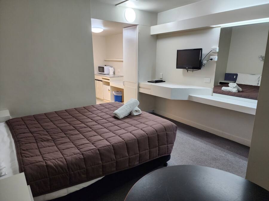 A hotel room with a bed, a small table, a mirror, a TV, and a kitchenette area.