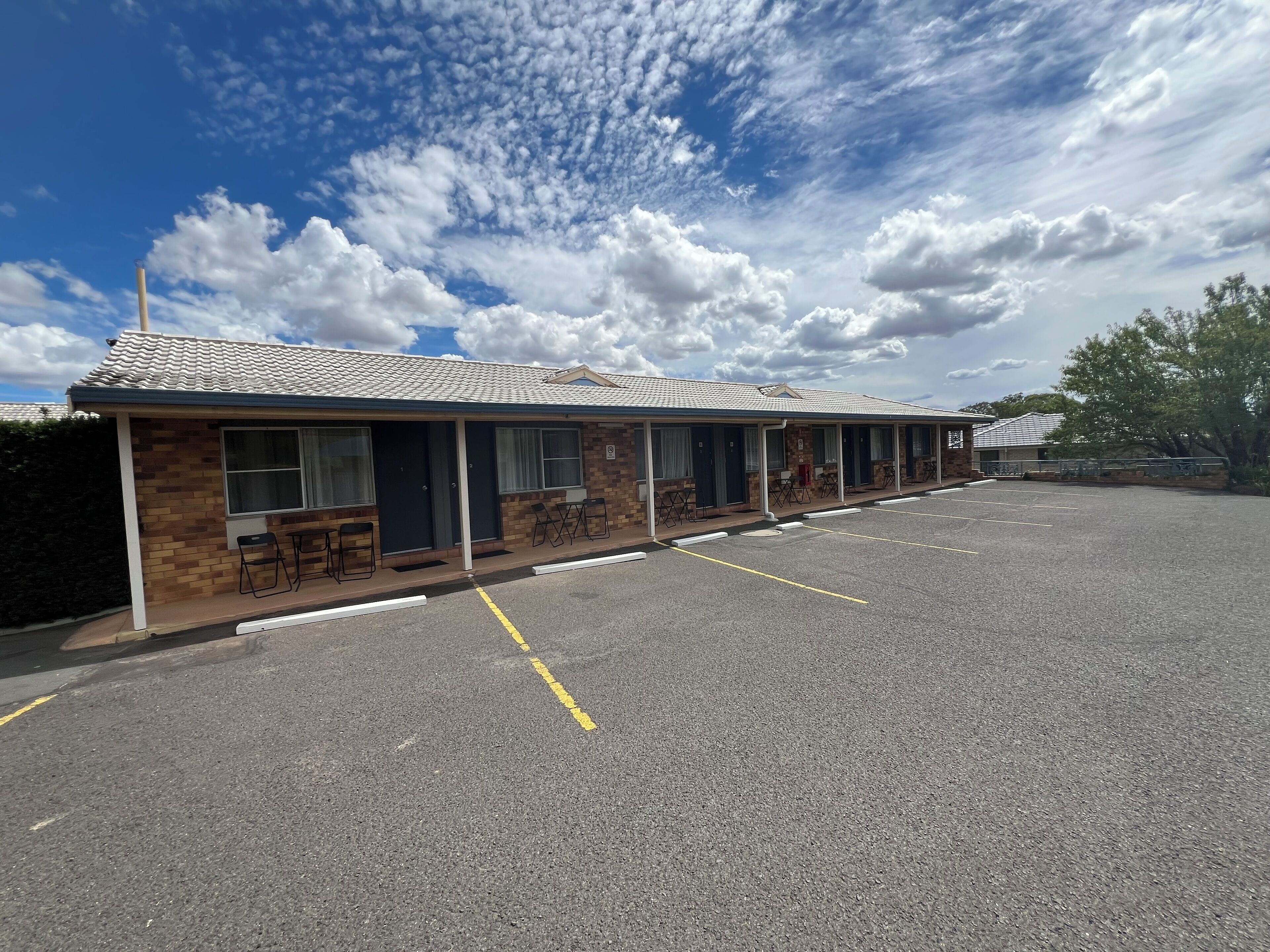 A motel with a row of rooms, a parking lot, and a clear sky.