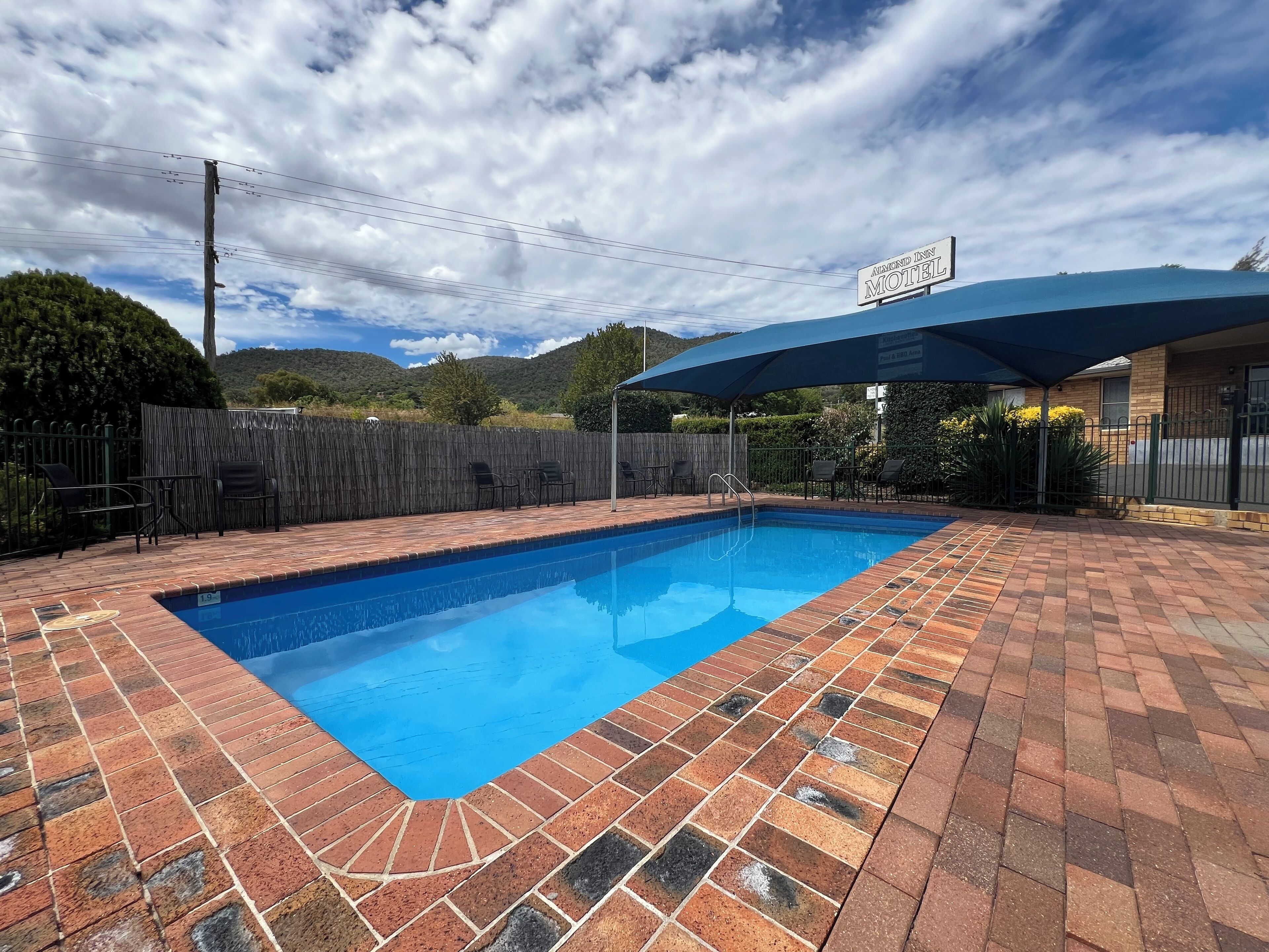 A swimming pool with a brick patio, a covered seating area, and a sign for the "Almond Inn Motel".
