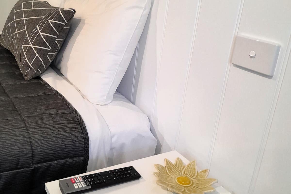 A neatly made bed with a black and white pillow, a remote control, and a decorative flower on a white nightstand.