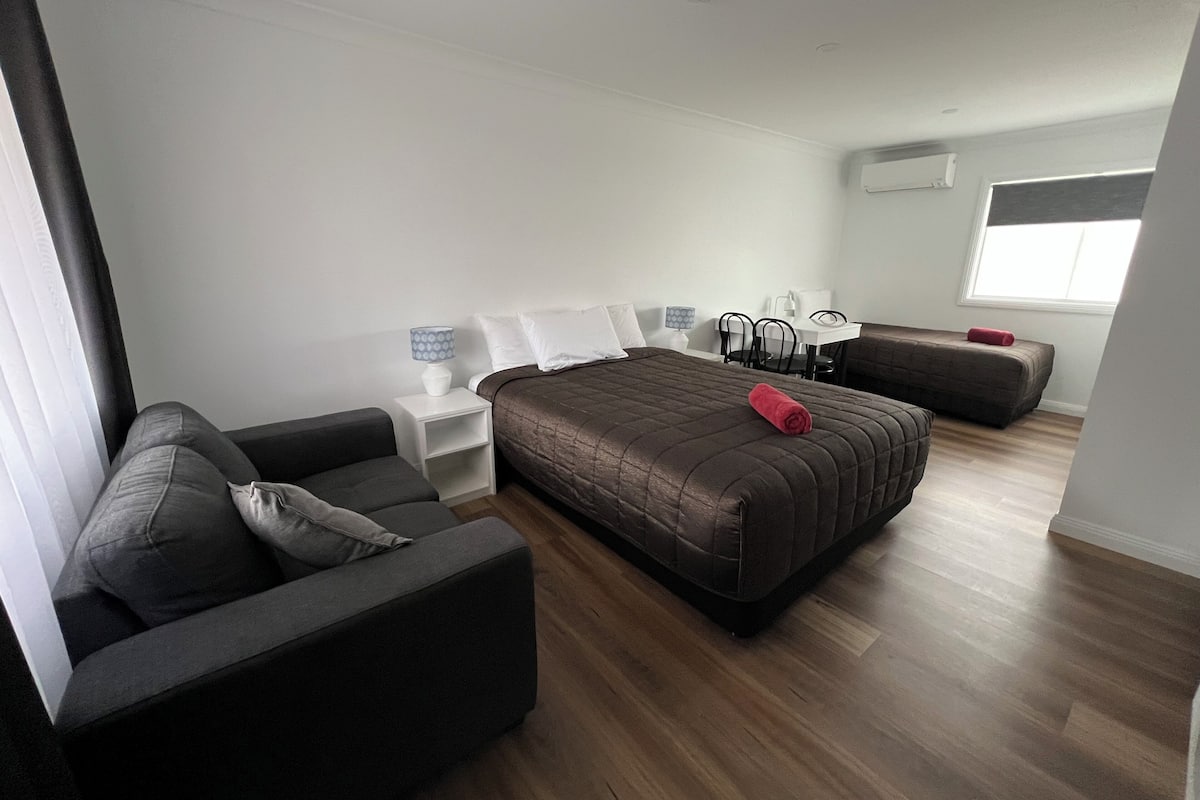 A modern hotel room with a large bed, a sofa, a desk, and a chair.