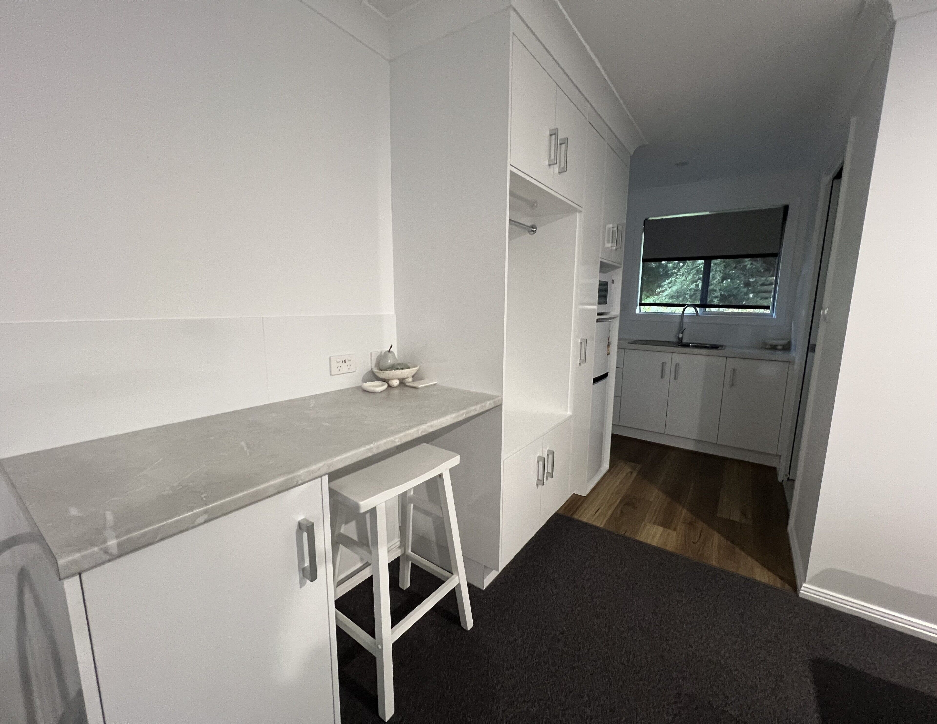 A modern kitchen with white cabinets, a grey countertop, and a small stool.