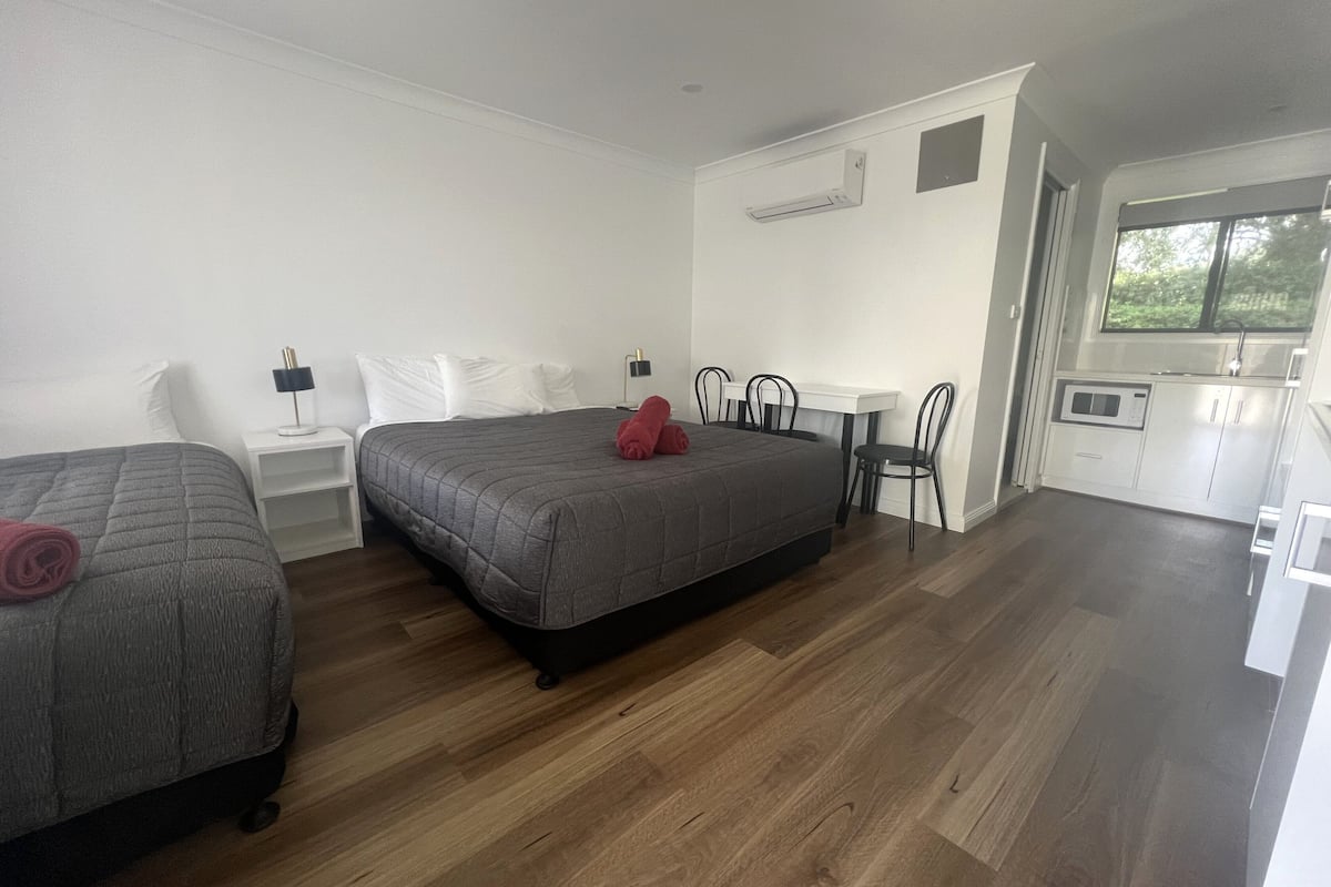 A hotel room with two beds, a small kitchenette, and a window.