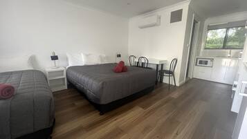 A hotel room with two beds, a small kitchenette, and a window.