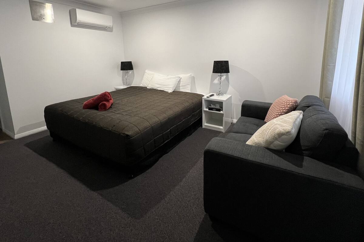 A hotel room with a bed, a sofa, a nightstand, and a lamp.