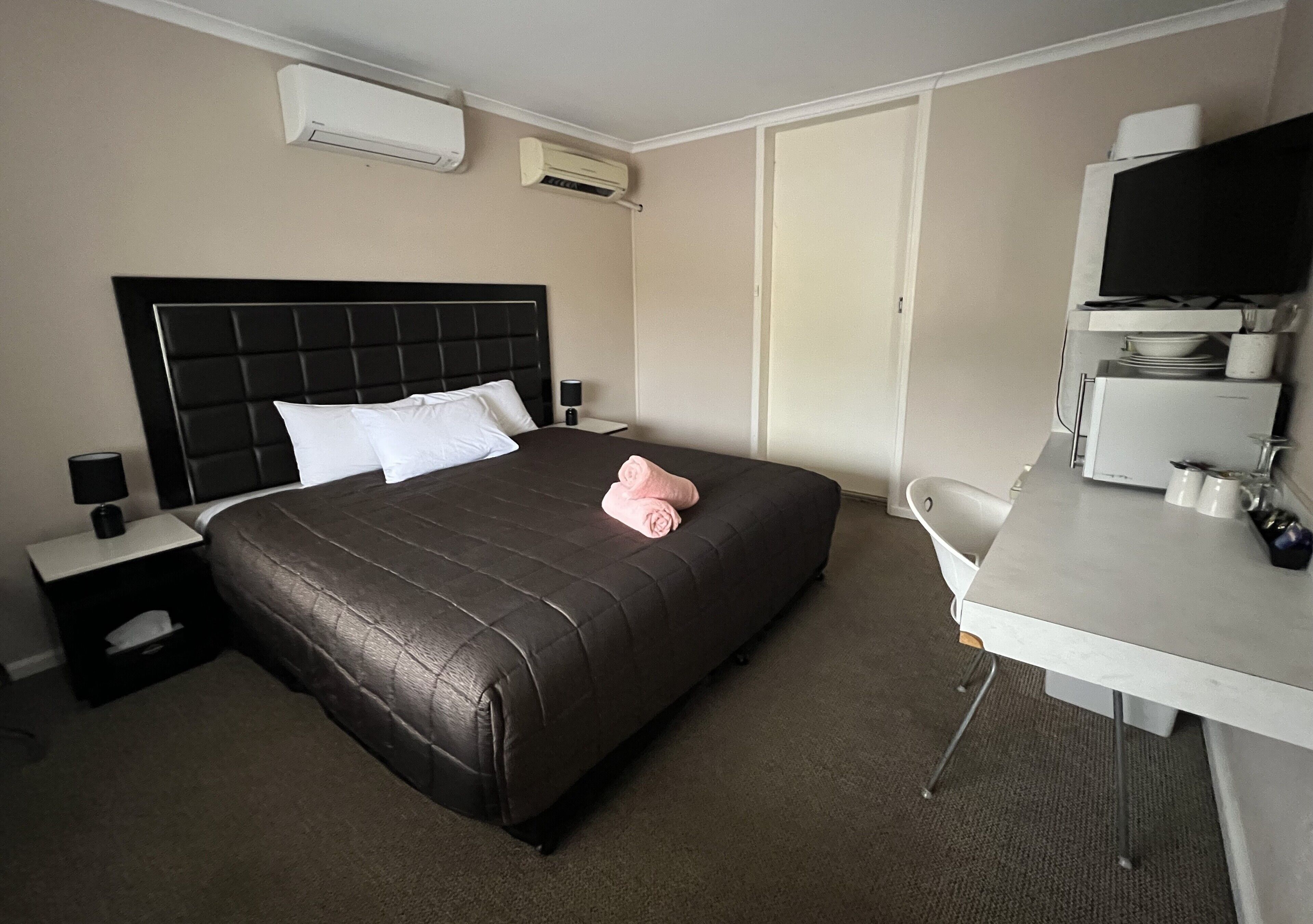 A hotel room with a large bed, a desk, a chair, and a television.