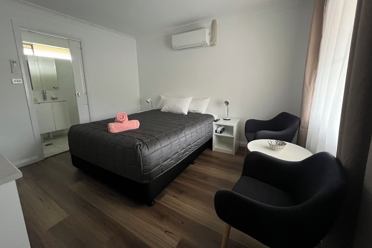A hotel room with a bed, bedside table, chair, and a small table with a bowl.