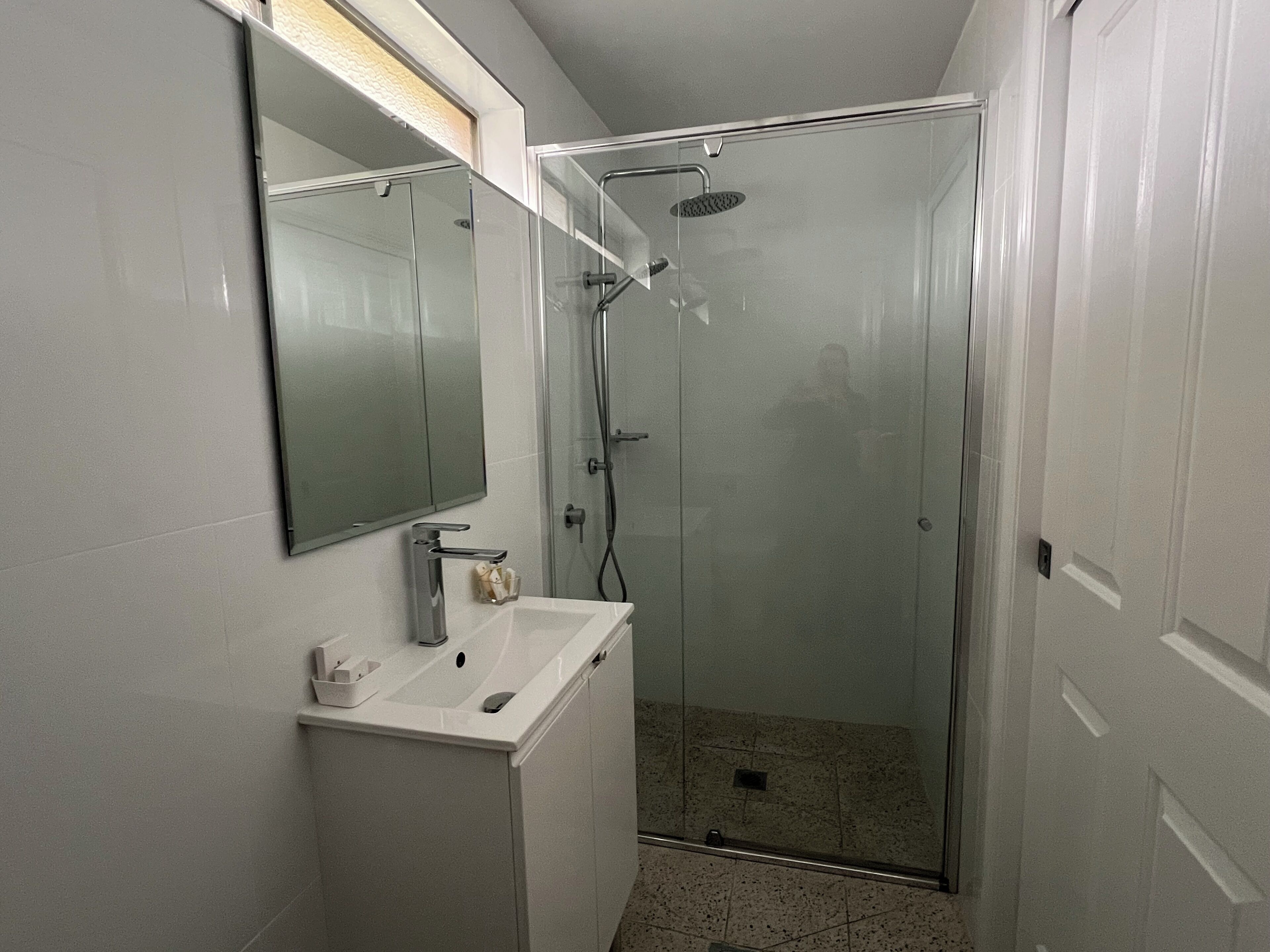 A modern bathroom with a glass-enclosed shower, a white sink, and a mirror above it.
