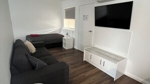 A modern living room with a sofa, a small table, and a TV mounted on the wall. - Almond Inn Motel (East Tamworth)