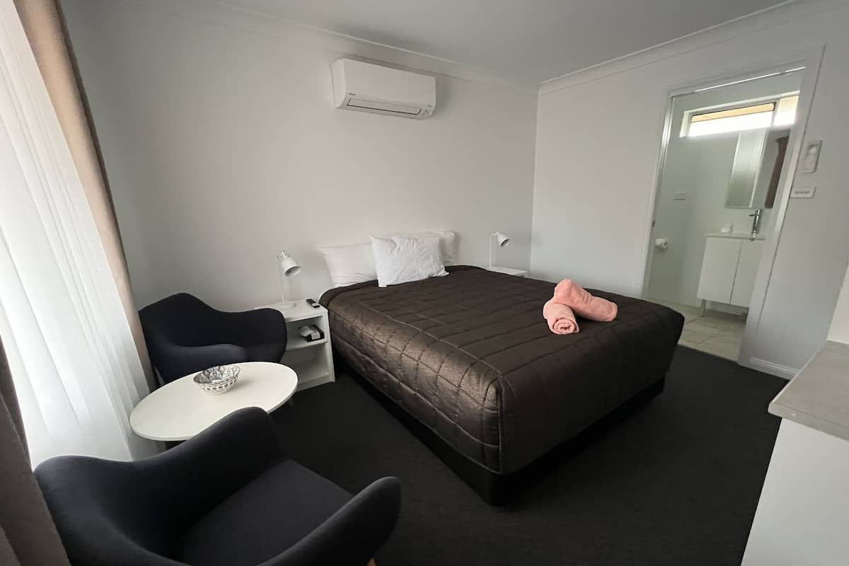 A hotel room with a bed, a desk, a chair, and a small table.