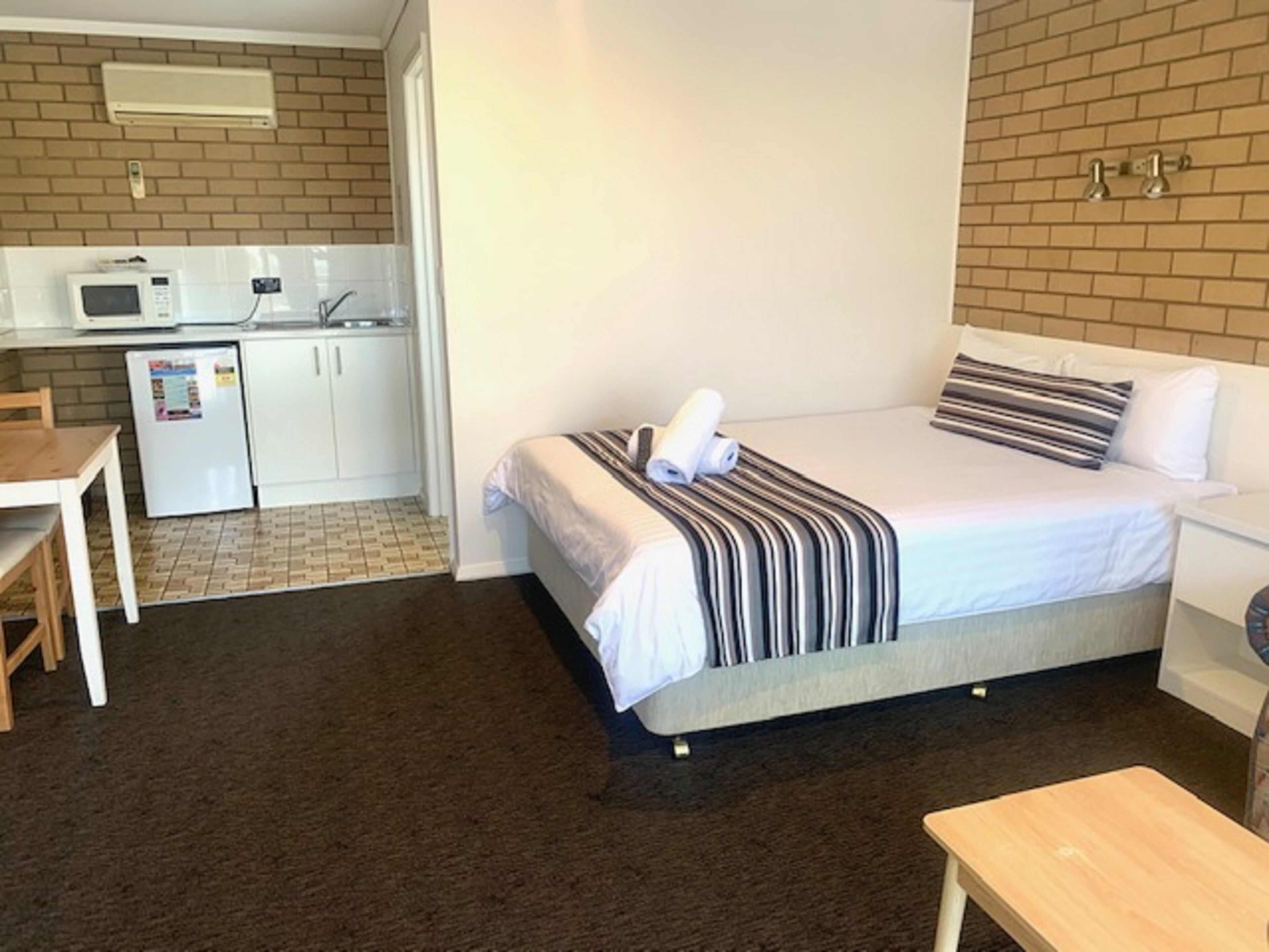 Una habitación de hotel compacta con una cama, un escritorio pequeño, un refrigerador y un microondas en la zona de kitchenette.
