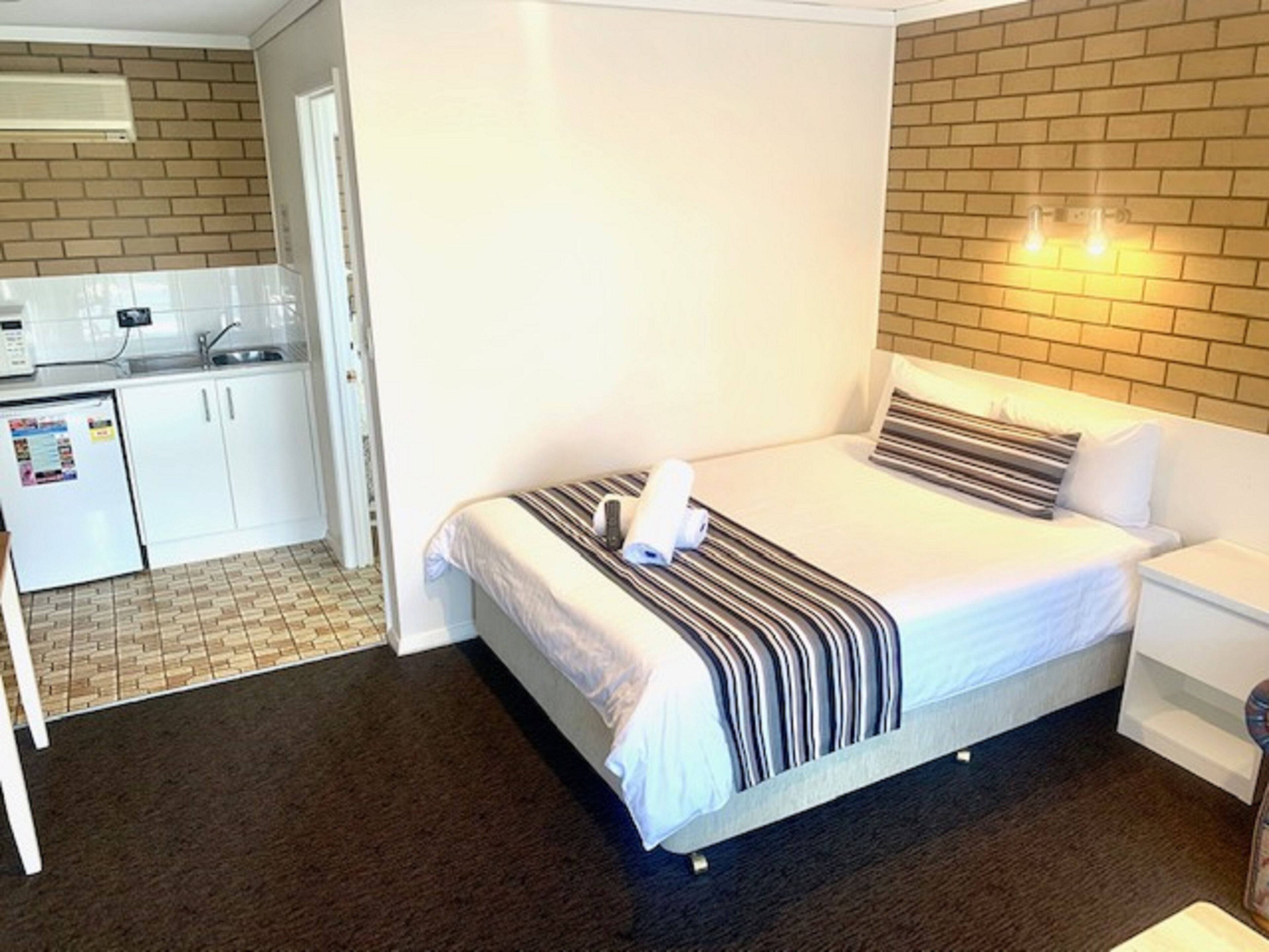 Habitación de hotel con cama, mesita de noche, un pequeño escritorio con silla, kitchenette y baño.