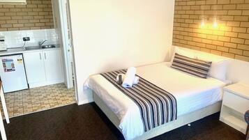 Habitación de hotel con cama, mesita de noche, un pequeño escritorio con silla, kitchenette y baño.