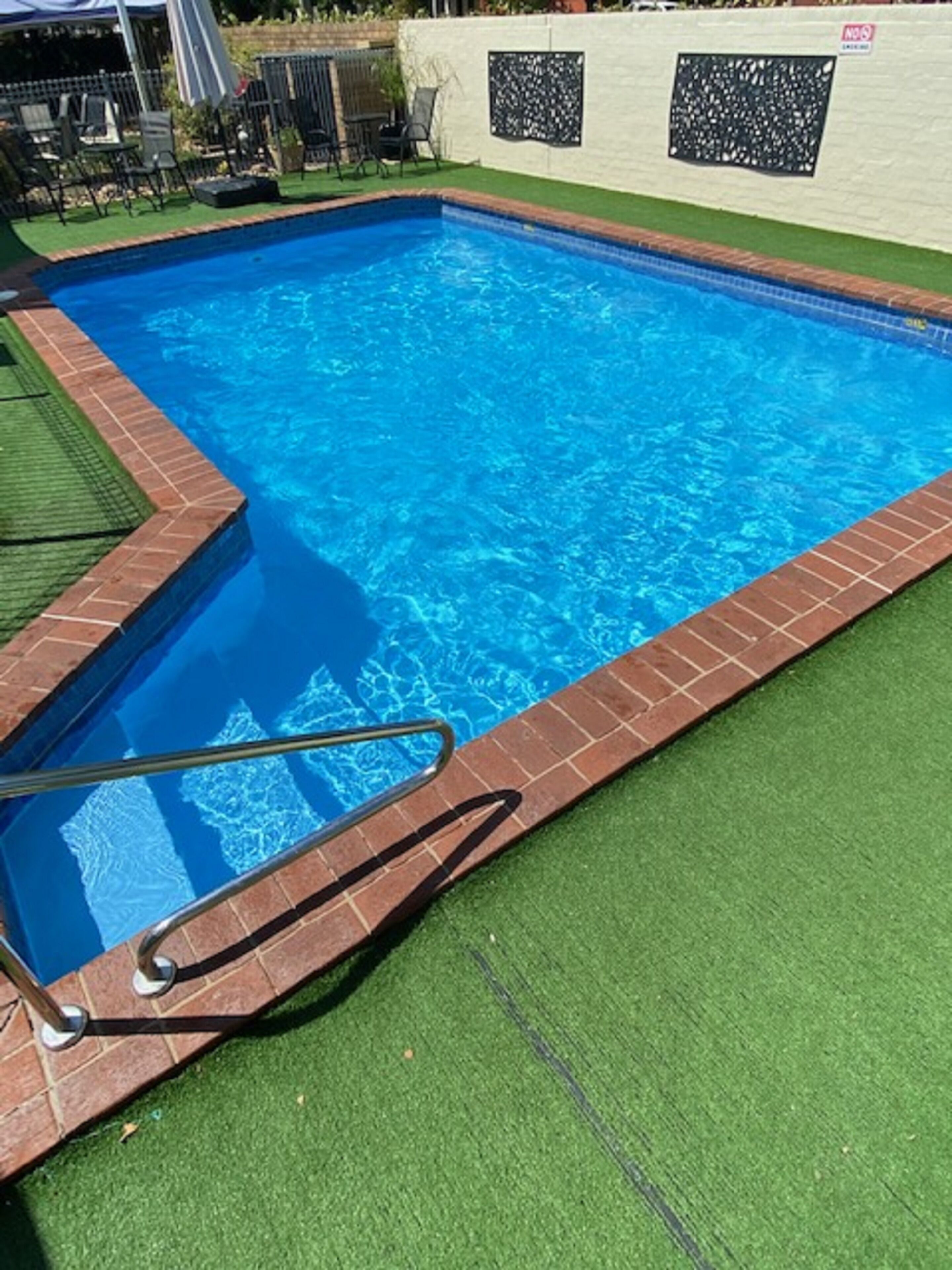 Una piscina rectangular con borde de ladrillo y escalera metálica.