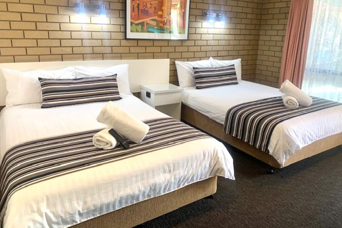 A hotel room with two beds, each with striped bedding and pillows, a nightstand, a framed picture on the wall, and a window with curtains.