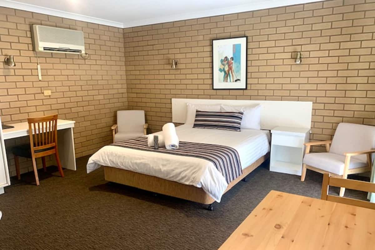 A hotel room with a bed, two chairs, a desk, and a picture on the wall.