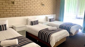 Habitación de hotel con dos camas individuales, una pared de ladrillo, una ventana con cortinas y una mesita de noche con lámpara.