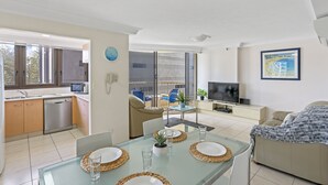A modern living room with a glass dining table, sofa, and TV.