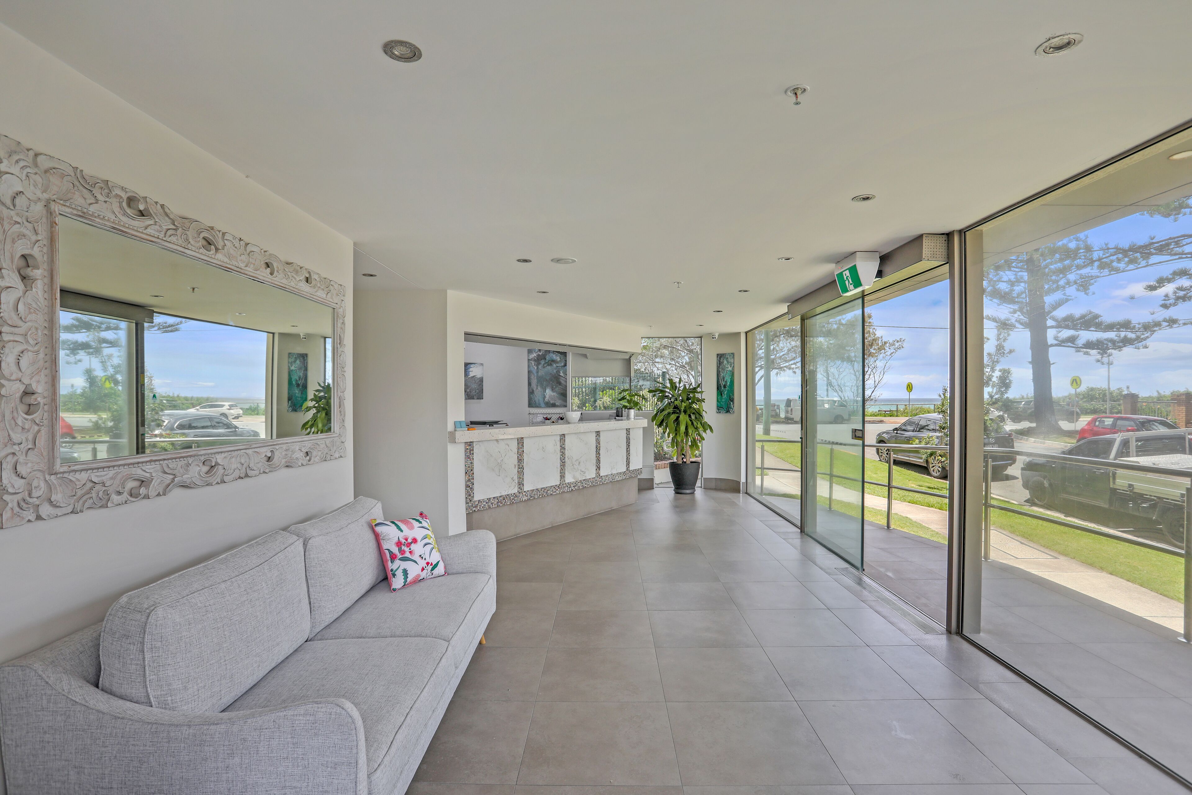 A modern lobby with a grey sofa, a reception desk, and large windows offering a view of the outdoors.