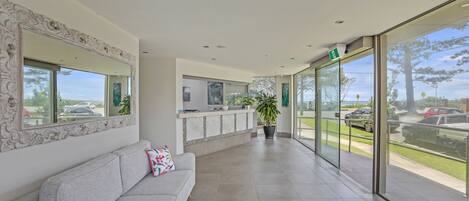A modern lobby with a grey sofa, a reception desk, and large windows offering a view of the outdoors.