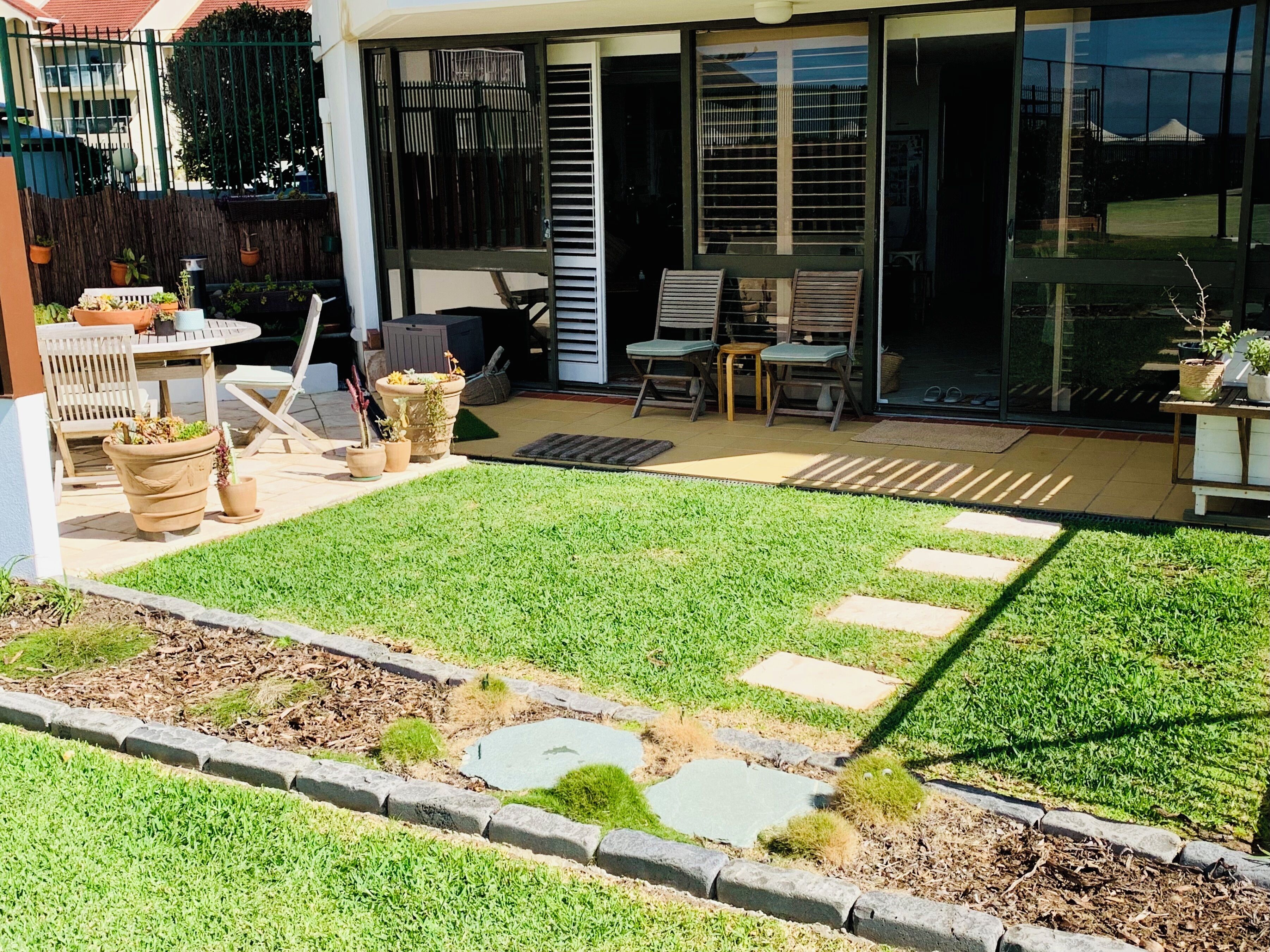 A well-maintained backyard with a lawn, potted plants, outdoor furniture, and a patio area.