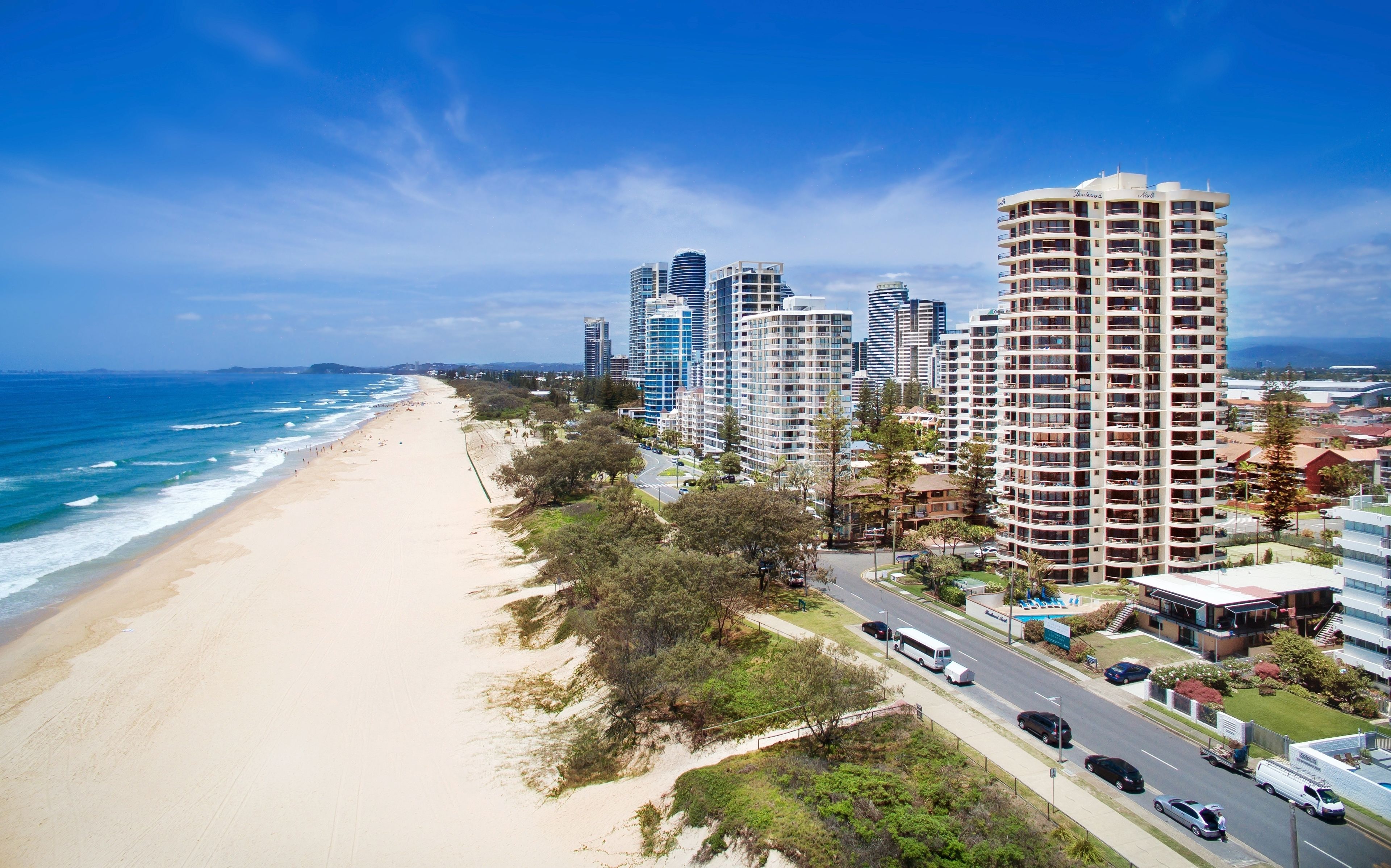 A coastal cityscape with a beach, high-rise buildings, and a road with vehicles.