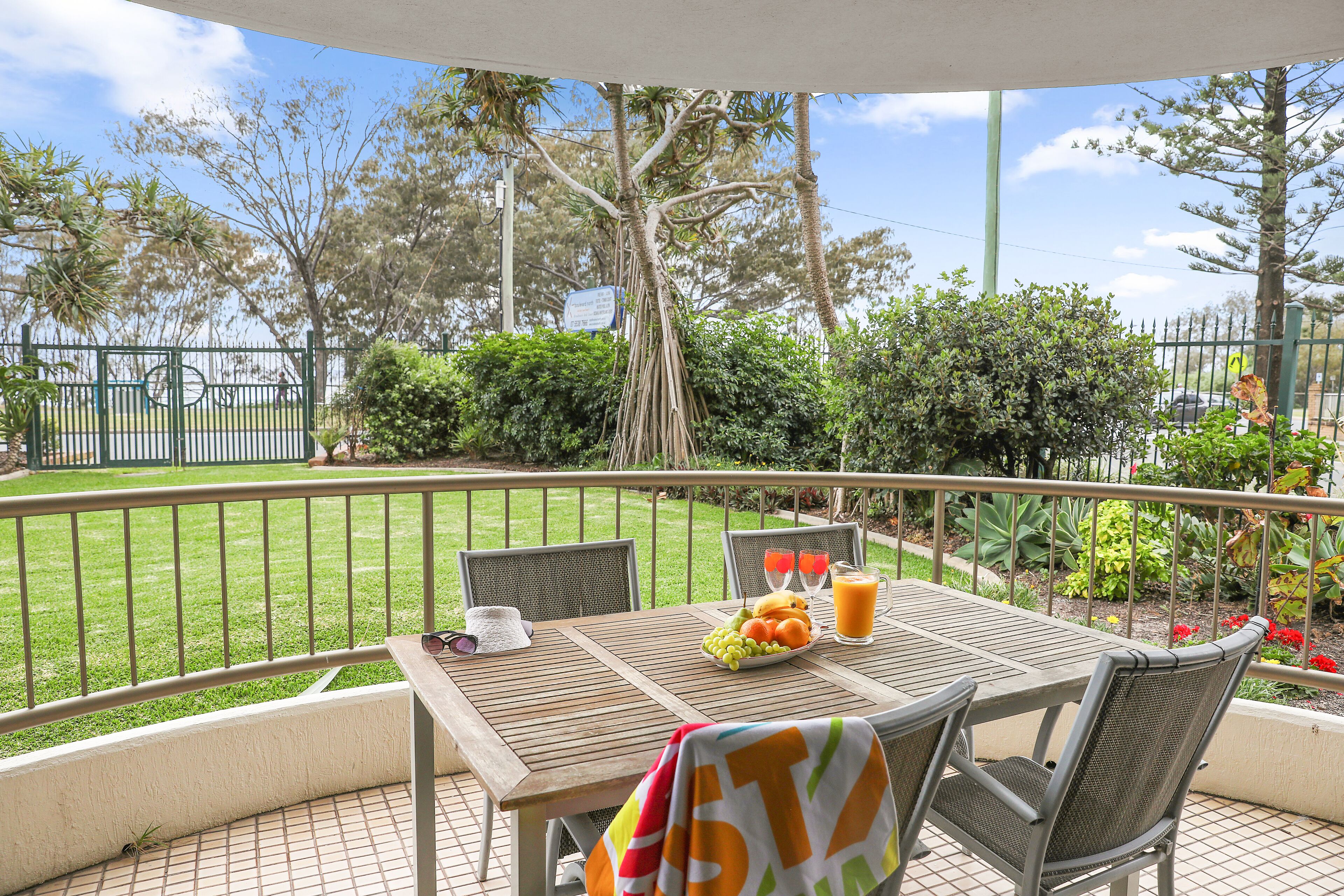 Un patio exterior con una mesa lista para dos personas, rodeado de sillas, un pequeño jardín y vistas a la calle.