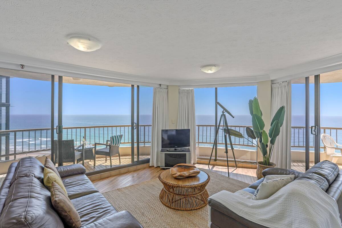 Een ruim balkon met uitzicht op de oceaan, voorzien van een bank, een televisie en een eethoek.