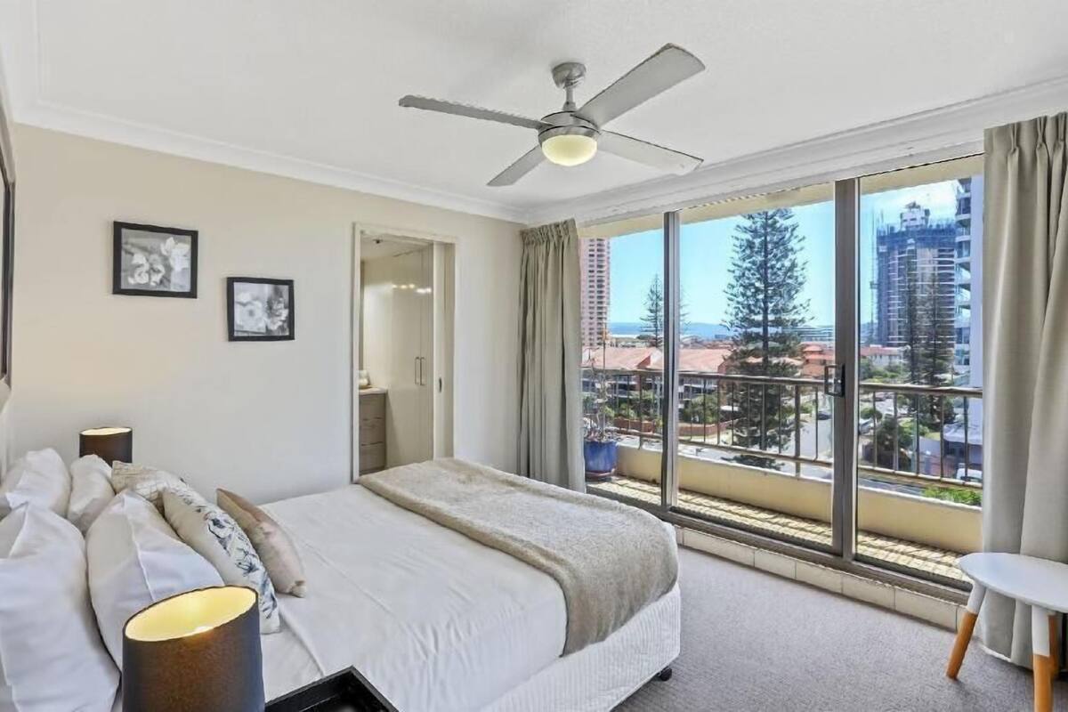Een hotelkamer met een bed, een plafondventilator, een groot raam met uitzicht over de stad en een balkon.