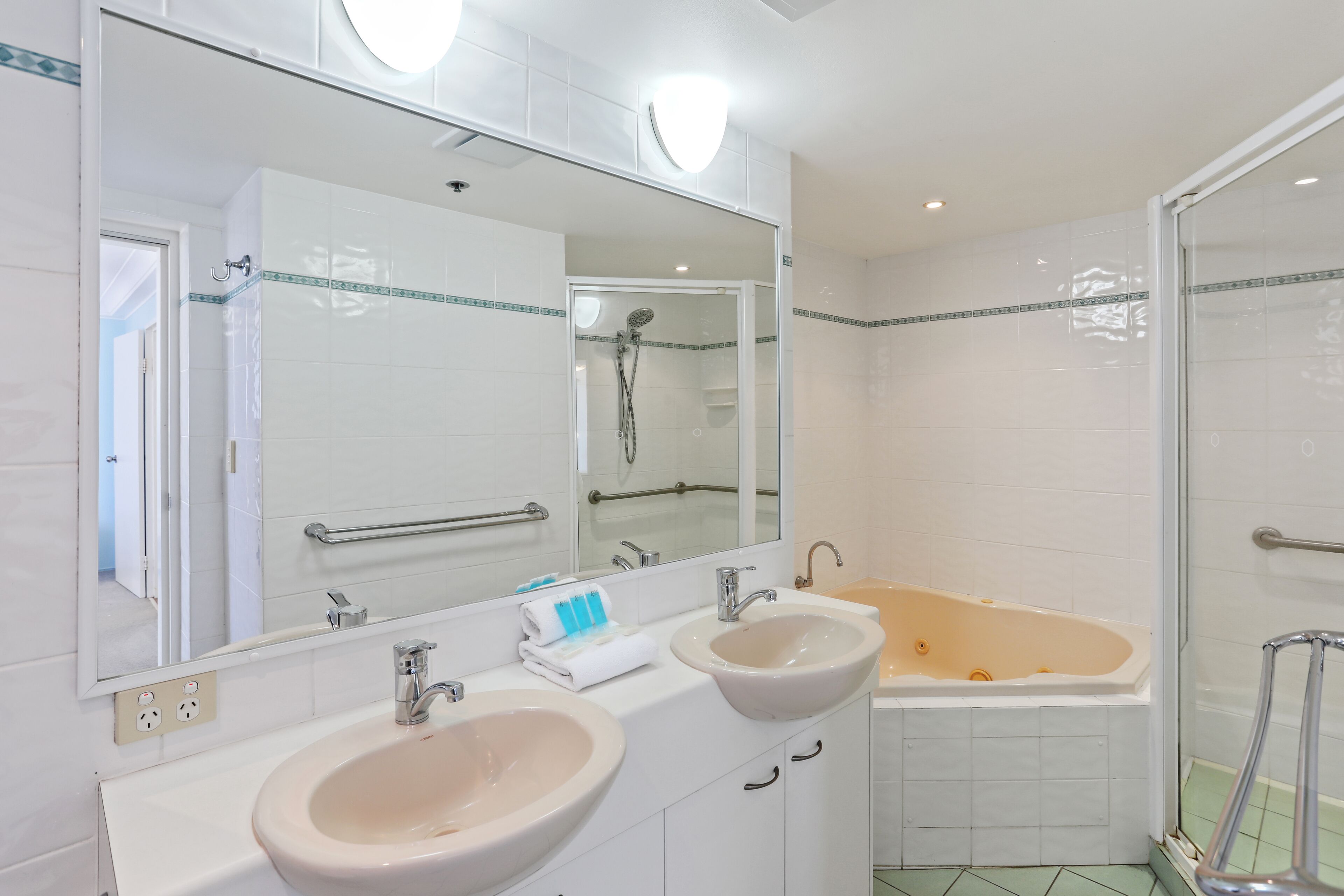 Un baño con dos lavamanos, un espejo grande, una bañera y una cabina de ducha de vidrio.