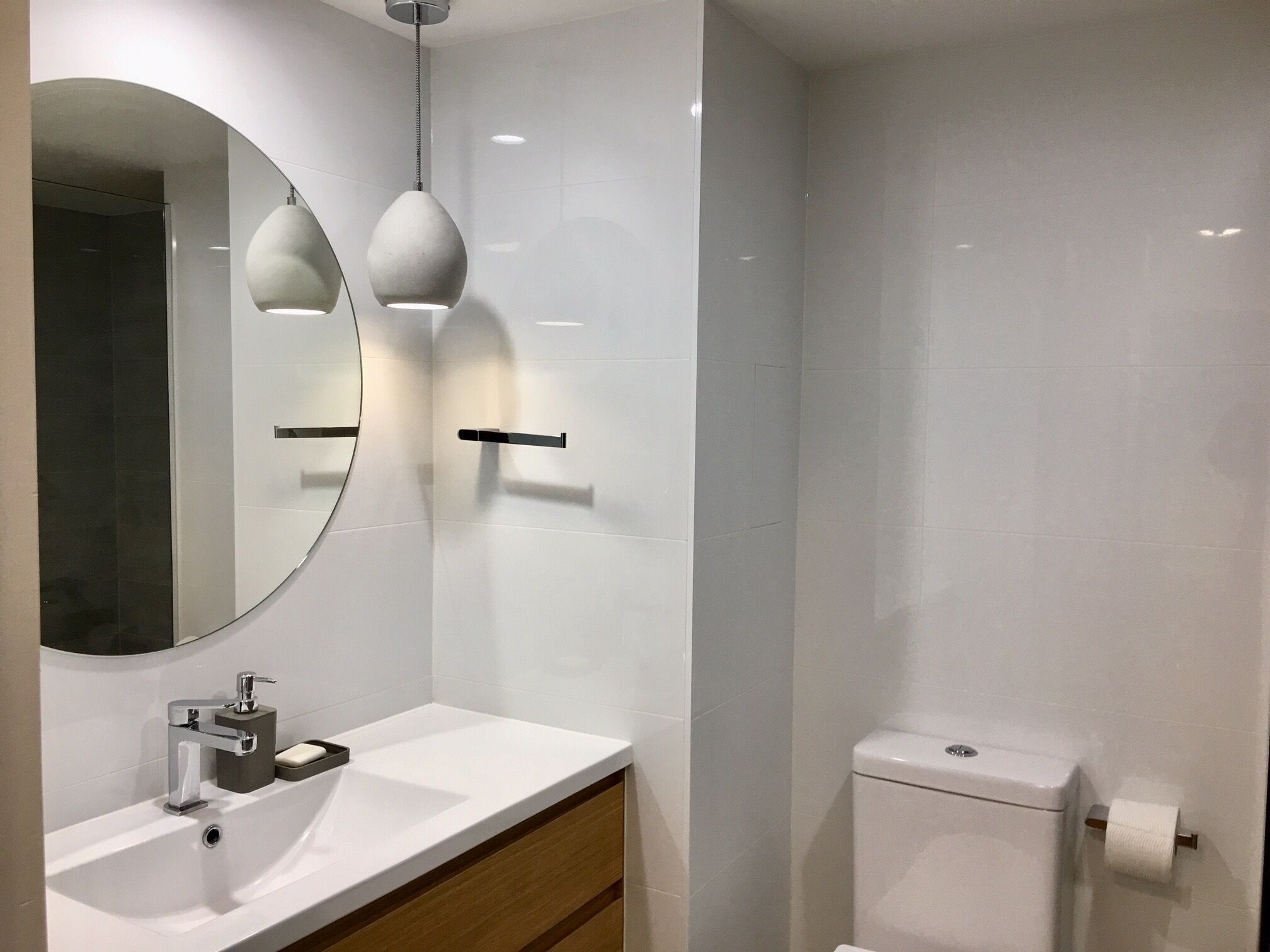 Un baño moderno con lavamanos, espejo e inodoro blancos.