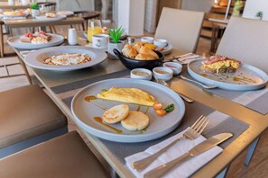 Un desayuno servido con platos de comida, incluyendo una tortilla, tostadas y pasteles, sobre una mesa con posavasos.