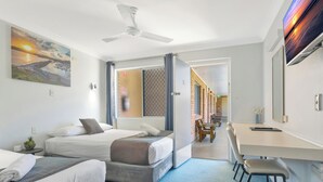Habitación de hotel con dos camas, un escritorio y una silla. Cuenta con un ventilador de techo y un cuadro en la pared.