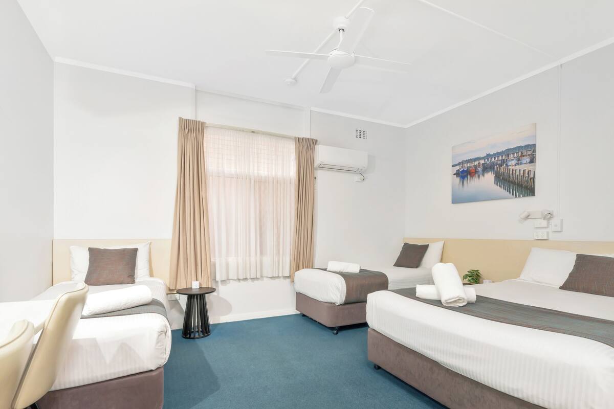 A hotel room with two beds, a chair, a small table, and a painting on the wall.