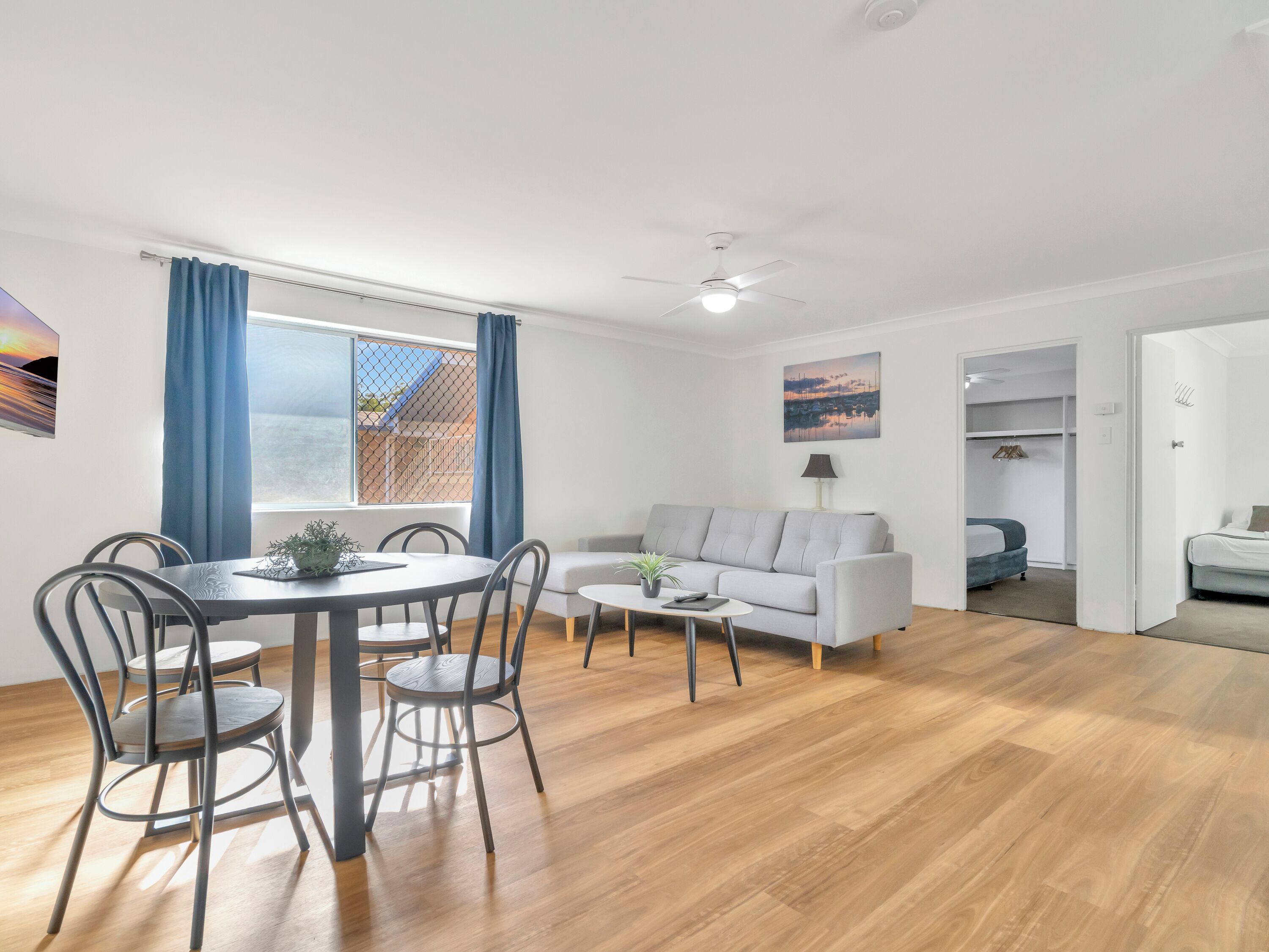 Ein modernes Wohnzimmer mit Essbereich, einem grauen Sofa, einem Couchtisch und einem Deckenventilator.