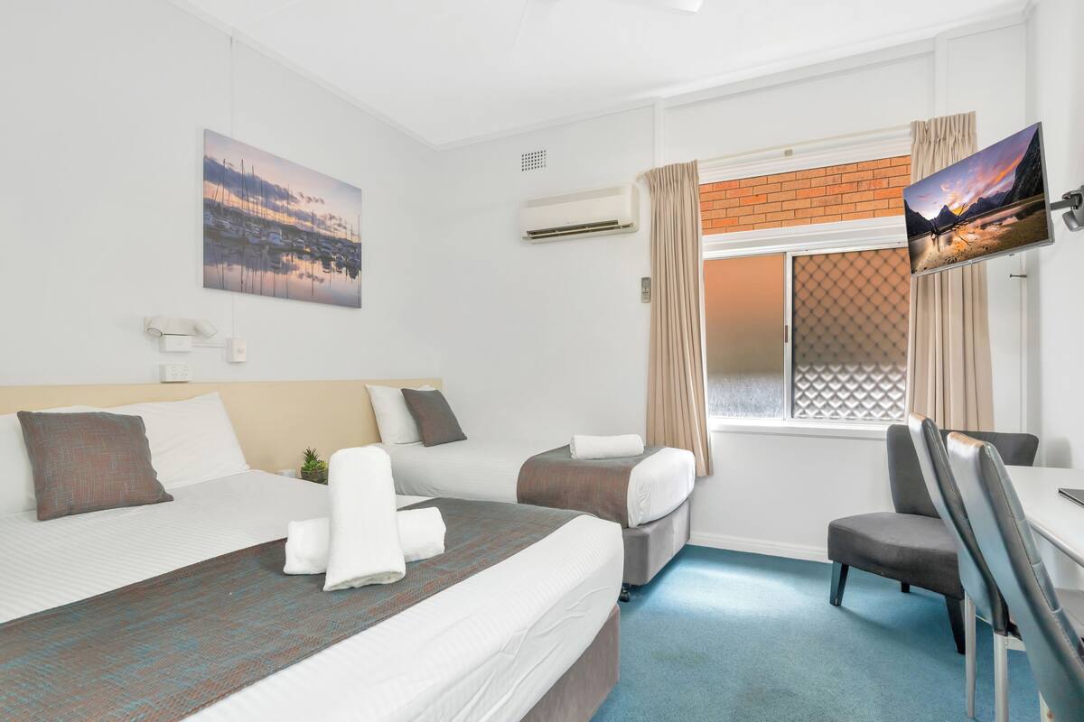 A hotel room with a large bed, a desk with a chair, a TV, and a window with curtains.