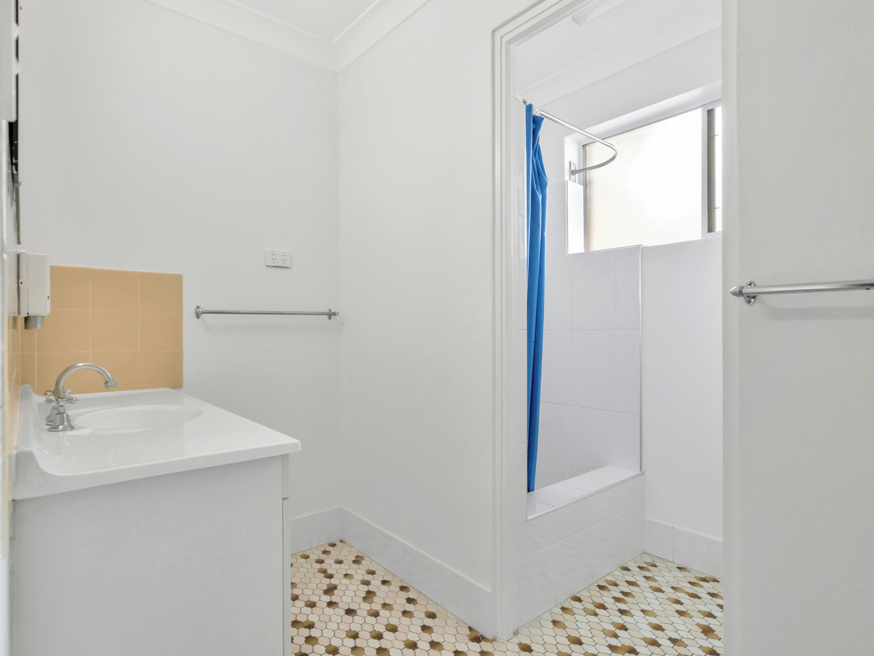 Un baño con un lavamanos blanco, una ducha con cortina azul y suelo de baldosas con un diseño geométrico.