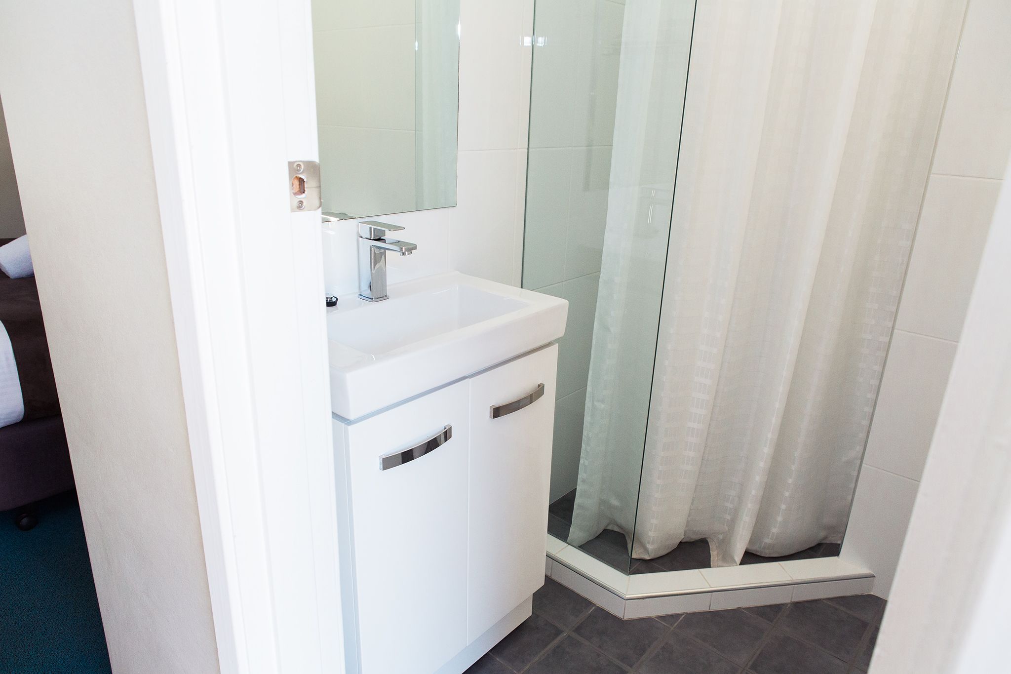 A modern bathroom with a white sink, mirror, and shower area.