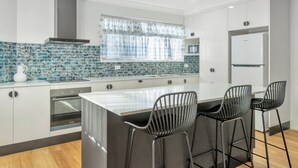 Una cocina moderna con una isla central, taburetes de bar, horno empotrado y refrigerador.