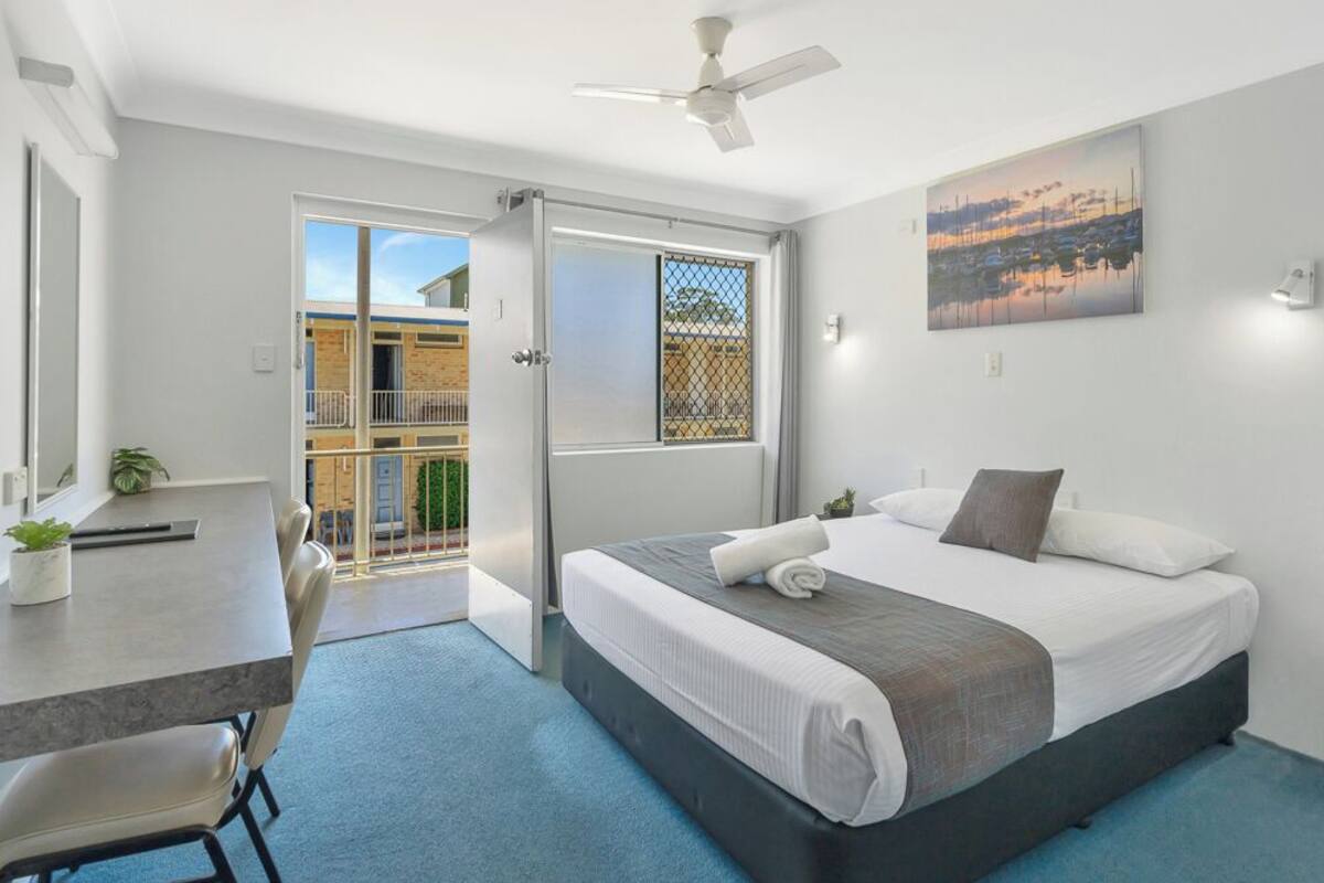 A bedroom with a bed, a desk, a chair, a ceiling fan, and a balcony door.