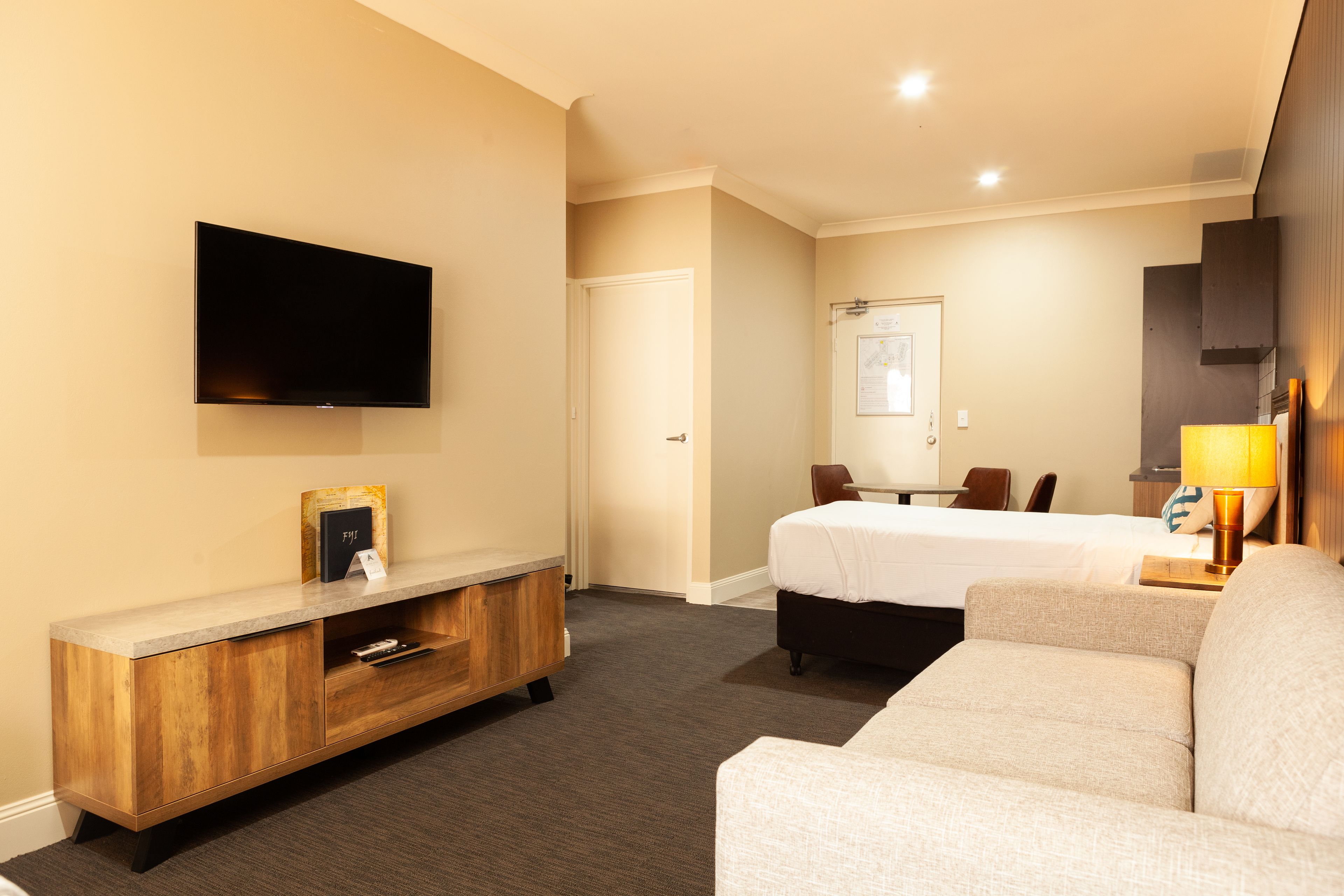 Une chambre d’hôtel équipée d’un téléviseur à écran plat fixé au mur, d’une console en bois, d’un lit recouvert d’une couette blanche, d’un canapé et d’un bureau avec une lampe.
