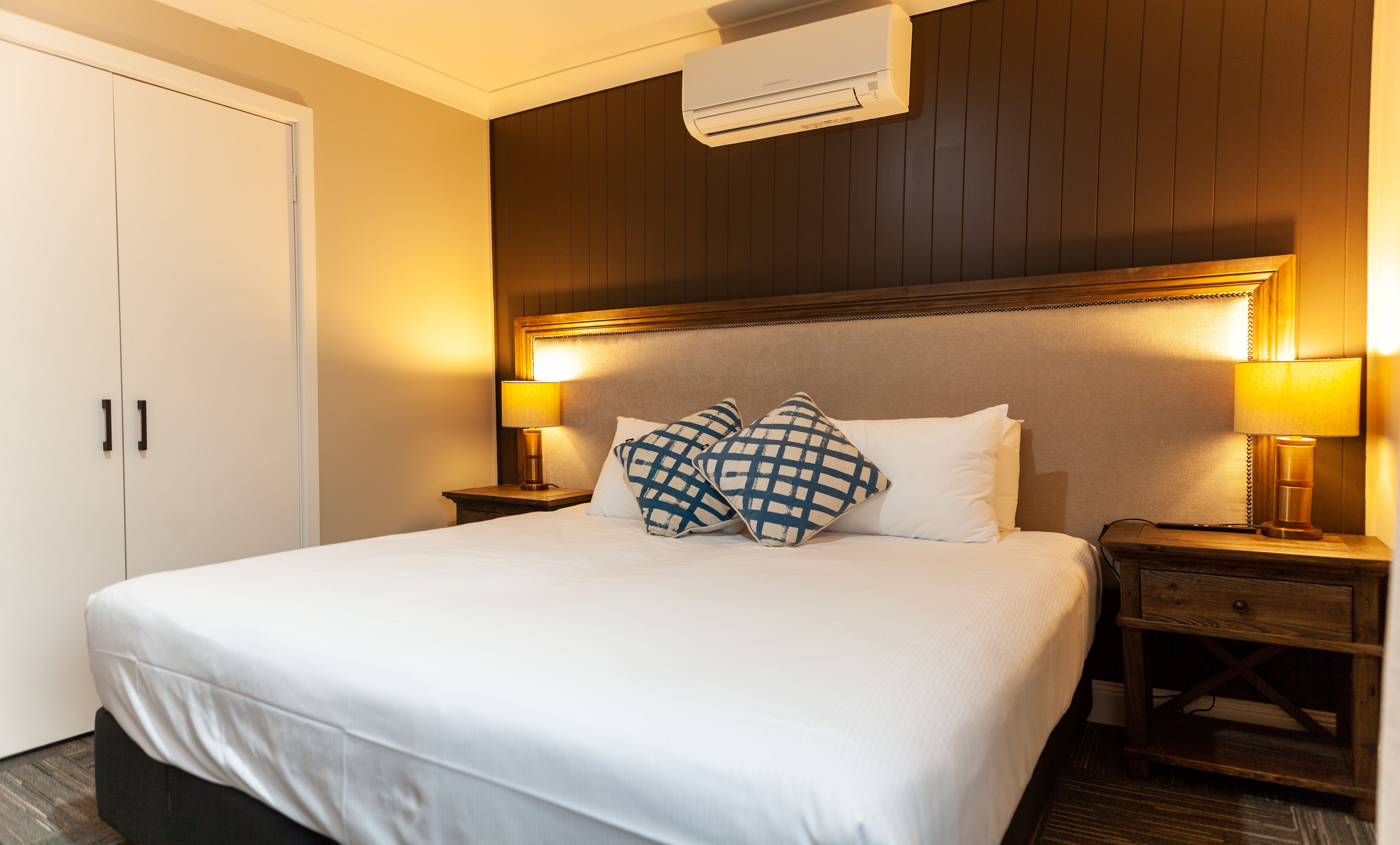 Habitación de hotel con una cama grande, dos mesitas de noche con lámparas, un armario y un equipo de aire acondicionado.