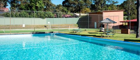 A swimming pool with a fenced area, a picnic table, and a small pavilion.